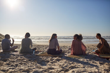 Yoga class talking on sunny beach during yoga retreat - CAIF22989