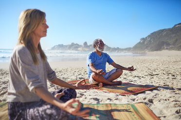 Gelassene Menschen meditieren am sonnigen Strand während eines Yoga-Retreats - CAIF22991