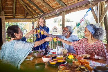 Freunde stoßen beim Frühstück in der Hütte während eines Yoga-Retreats mit Orangensaftgläsern an - CAIF23003