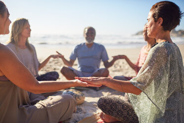 Serene people meditating in circle on sunny beach during yoga retreat - CAIF23011