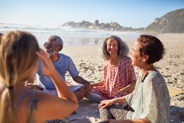 Friends sitting in circle on sunny beach during yoga retreat - CAIF23013