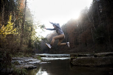 Seitenansicht eines Teenagers, der über einen Fluss gegen Bäume im Wald springt - CAVF61743