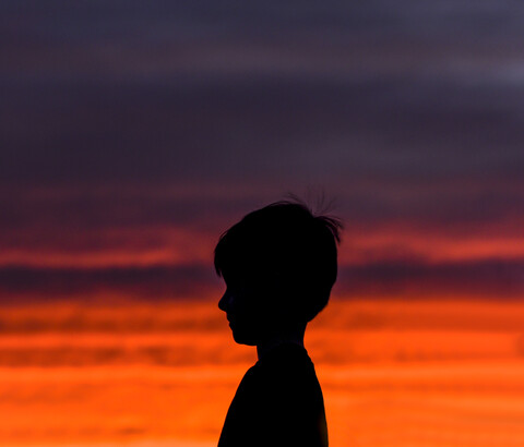 Seitenansicht der Silhouette Junge gegen dramatischen Himmel im Sonnenuntergang stehen, lizenzfreies Stockfoto