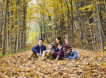 Verspielte Mutter sitzt mit Söhnen auf trockenen Blättern im Wald - CAVF61747