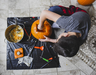 High angle view of boy removing seeds from pumpkin at home - CAVF61765