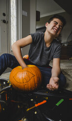 Boy removing seeds from pumpkin while sitting on floor at home - CAVF61766