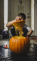 Boy removing seeds from fresh pumpkin at home - CAVF61767