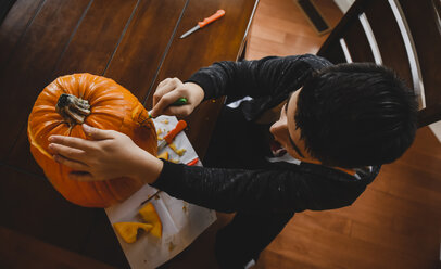 High angle view of boy making Jack O' Lantern at home during Halloween - CAVF61769
