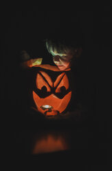 Junge betrachtet beleuchtete Jack-O'-Lantern in der Dunkelkammer während Halloween - CAVF61770