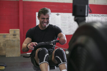 Confident male adaptive athlete exercising with rowing machine against wall in gym - CAVF61771