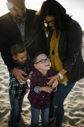 Glückliche Eltern, die mit ihren Söhnen am Strand spielen, während sie an einem sonnigen Tag stehen - CAVF61783