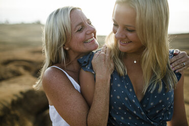 Happy mother embracing daughter while standing on cliff against sky during sunset - CAVF61784