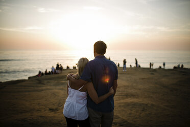 Rückansicht eines Paares, das auf das Meer blickt, während es auf einer Klippe gegen den Himmel bei Sonnenuntergang schleift - CAVF61793