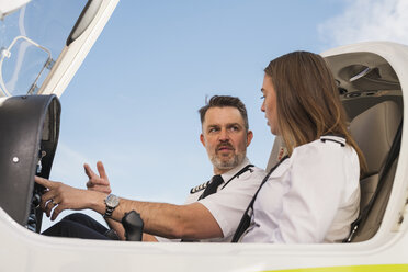 Low angle view of male pilot teaching trainee to operate control panel in airplane against blue sky at airport - CAVF61798