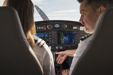 Rear view of male pilot showing dashboard to female trainee in airplane at airport - CAVF61799