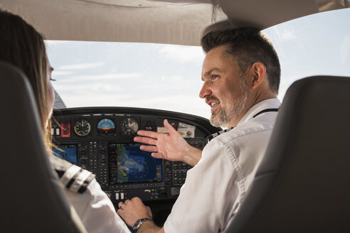 Rückansicht eines männlichen Piloten, der einer weiblichen Auszubildenden die Bedienung des Steuerpults in einem Flugzeug am Flughafen beibringt - CAVF61800