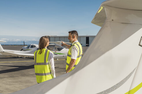 Seitenansicht eines männlichen Ingenieurs, der eine weibliche Auszubildende auf der Start- und Landebahn eines Flughafens vor blauem Himmel anleitet - CAVF61801