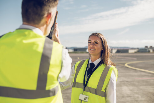 Rückansicht eines männlichen Ingenieurs, der einer weiblichen Auszubildenden Flugzeugteile zeigt, während er auf der Start- und Landebahn eines Flughafens vor blauem Himmel steht - CAVF61802