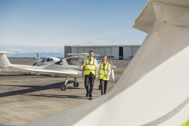 Männlicher Ingenieur mit weiblicher Auszubildender geht gegen den blauen Himmel auf der Start- und Landebahn eines Flughafens an einem sonnigen Tag - CAVF61803