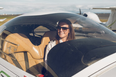 Lächelnde Pilotin mit Sonnenbrille im Flugzeug sitzend durch die Windschutzscheibe gesehen - CAVF61811