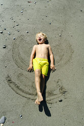 High angle view of happy shirtless boy making sand angel at beach during sunny day - CAVF61842