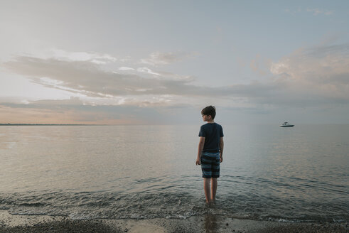 Rückansicht eines am Ufer stehenden Jungen gegen den Himmel bei Sonnenuntergang - CAVF61845