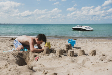 Shirtless boy making sandcastles at beach during sunny day - CAVF61851