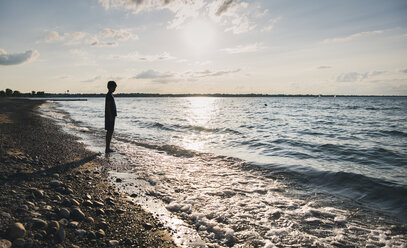 Full length of silhouette boy standing on shore at beach against sky during sunset - CAVF61853
