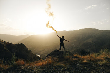 Rear view of silhouette man holding distress flare while standing on mountain against sky during sunset - CAVF61895