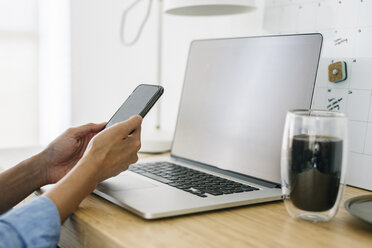 Cropped hands of businesswoman with laptop computer on desk using mobile phone in office - CAVF61898