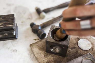 Abgeschnittene Hände einer Juwelierin beim Hämmern eines Schlagstempels auf einen Doming-Block in einer Werkstatt - CAVF61942
