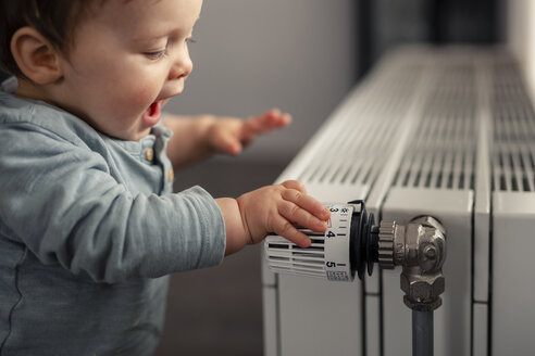 Excited baby boy playing with thermostat of heater - SEBF00020