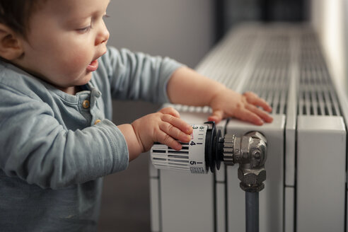 Baby boy playing with thermostat of heater - SEBF00021