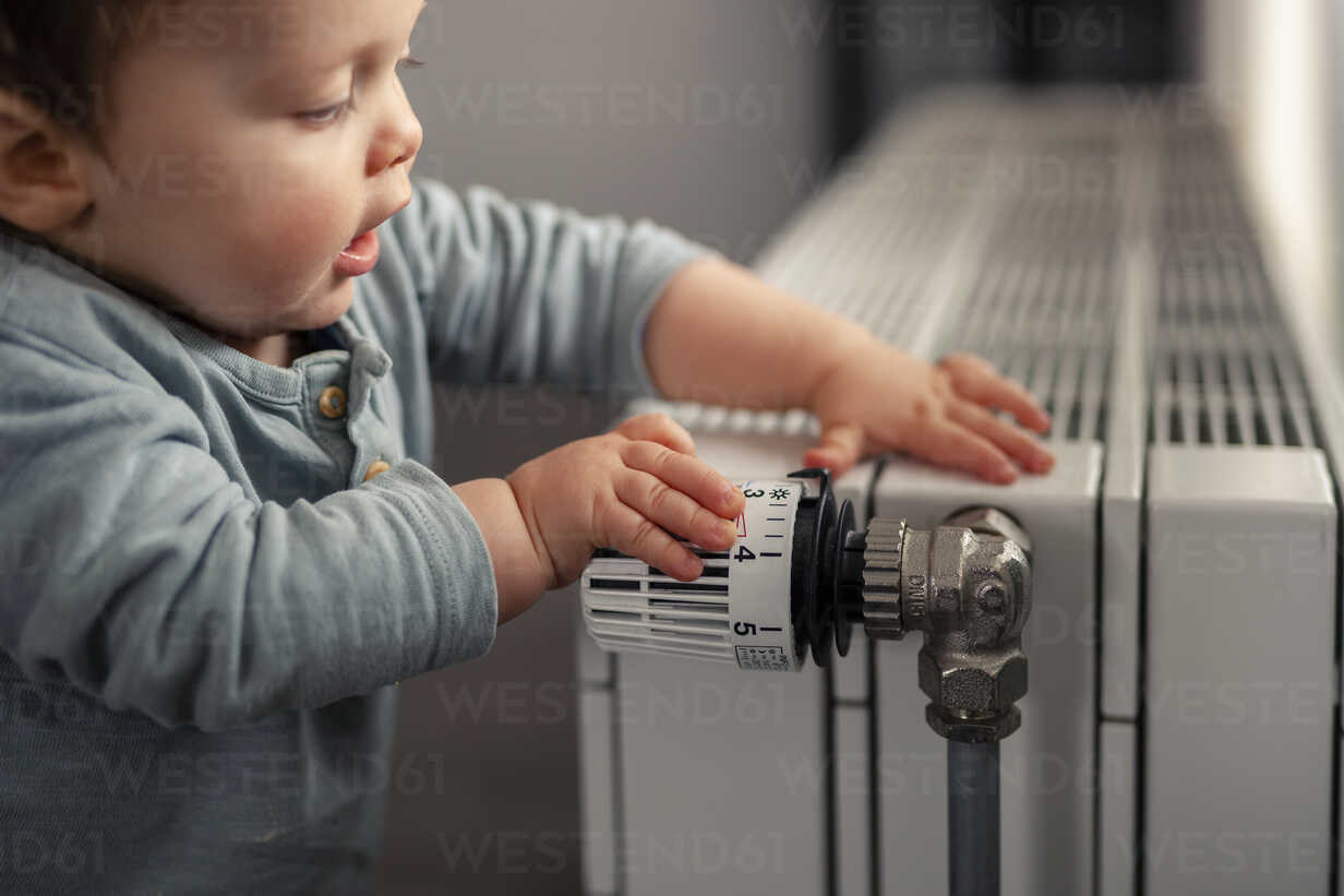Baby boy playing with thermostat of heater stock photo