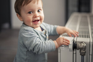 Porträt eines lächelnden kleinen Jungen, der mit dem Thermostat der Heizung spielt - SEBF00022