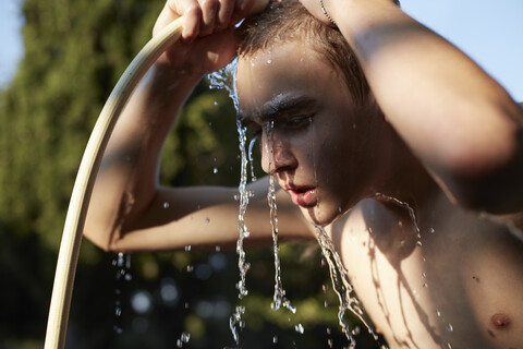Jugendlicher erfrischt sich mit Wasser aus dem Gartenschlauch, lizenzfreies Stockfoto