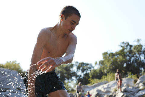 France, portrait of teenage boy bathing in lake splashing with water stock photo