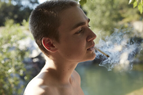 Portrait of teenage boy smoking cigarette in nature - AMEF00013