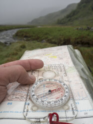 Großbritannien, Schottland, Knoydart Peninsula, Hand hält Kompass und Karte bei Regen - HUSF00023