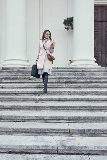 Österreich, Wien, junge Geschäftsfrau geht die Treppe hinunter und schaut auf ihr Handy - ZEDF01924