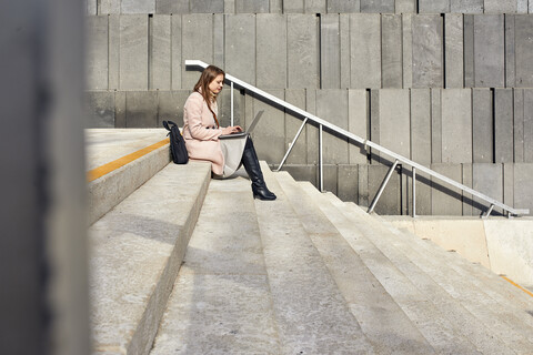 Österreich, Wien, junge Frau sitzt auf einer Treppe im MuseumsQuartier und benutzt einen Laptop, lizenzfreies Stockfoto