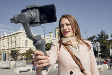 Österreich, Wien, Porträt einer lächelnden jungen Frau, die einen Selfie-Stick benutzt, um ein Foto mit ihrem Smartphone aufzunehmen - ZEDF01939
