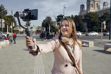 Österreich, Wien, Porträt einer lächelnden jungen Frau, die einen Selfie-Stick zum Fotografieren benutzt - ZEDF01940
