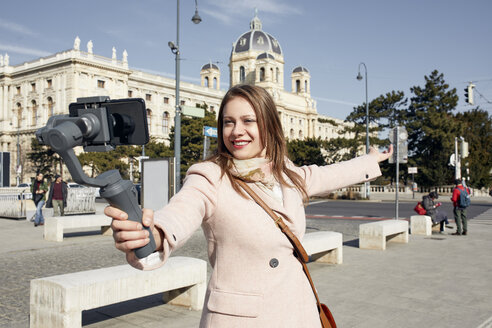 Österreich, Wien, Porträt einer lächelnden jungen Frau, die einen Selfie-Stick benutzt, um ein Foto mit ihrem Smartphone aufzunehmen - ZEDF01941