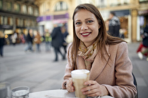 Österreich, Wien, Porträt einer lächelnden jungen Frau, die in einem Straßencafé Kaffee trinkt - ZEDF01943