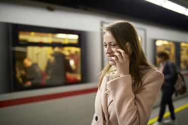 Österreich, Wien, lächelnde junge Frau am Telefon auf dem Bahnsteig einer U-Bahn-Station - ZEDF01946