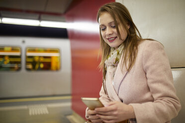 Austria, Vienna, portrait of smiling young woman at underground station looking at smartphone - ZEDF01949