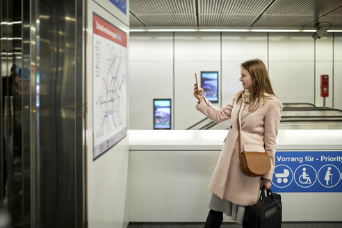 Österreich, Wien, junge Frau, die in einer U-Bahn-Station eine Karte fotografiert - ZEDF01952