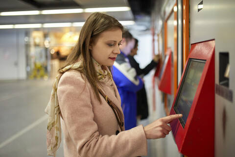 Österreich, Wien, junge Frau kauft Fahrkarte am Automaten am Bahnhof, lizenzfreies Stockfoto