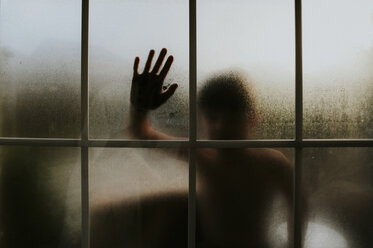 Boy touching wet window at home during sunset - CAVF61991